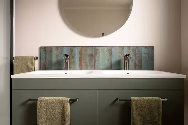 Double vanity with green tiles and round mirror